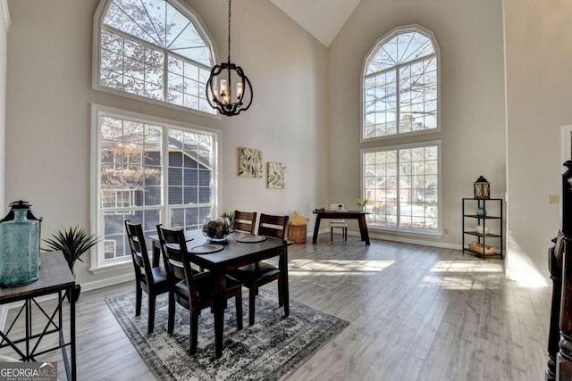 dining area with a notable chandelier, light wood-type flooring, and high vaulted ceiling