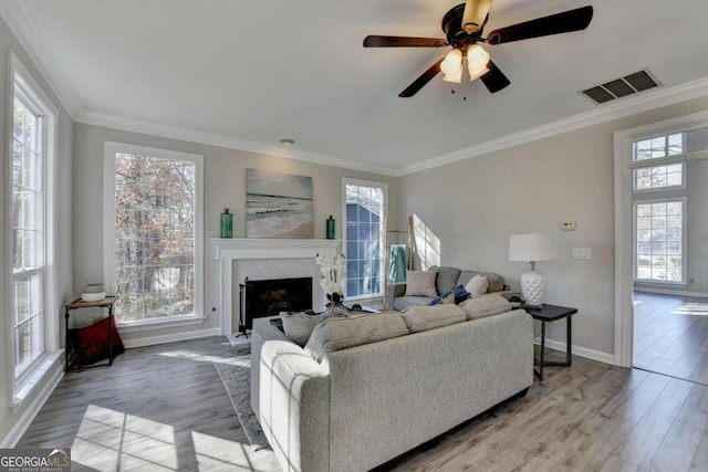 living room featuring a fireplace, ceiling fan, crown molding, and light hardwood / wood-style flooring