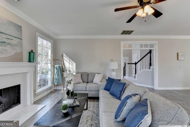 living room with a high end fireplace, light wood-type flooring, ceiling fan, and crown molding