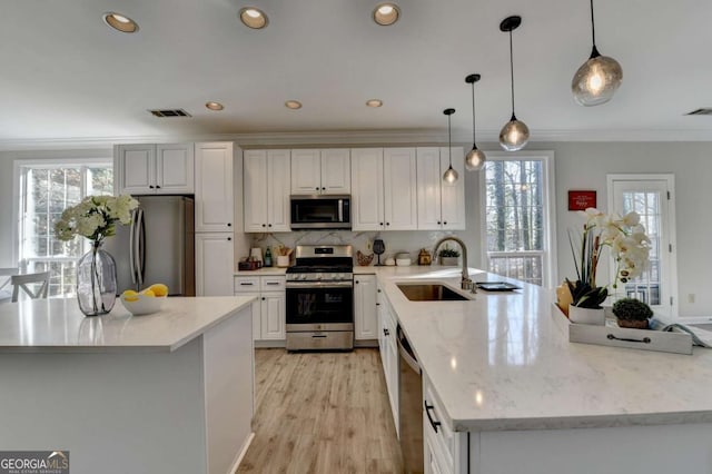 kitchen featuring light stone counters, hanging light fixtures, stainless steel appliances, white cabinetry, and sink