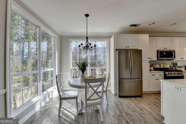 kitchen featuring stainless steel appliances, white cabinets, light wood-type flooring, hanging light fixtures, and a notable chandelier