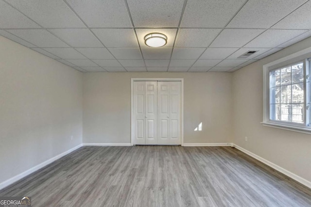 unfurnished bedroom with a paneled ceiling, a closet, and wood-type flooring