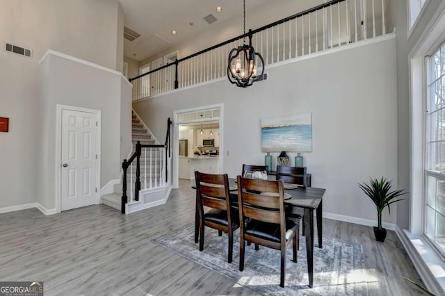 dining space featuring a towering ceiling, an inviting chandelier, and light wood-type flooring