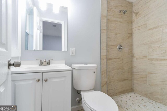 bathroom featuring toilet, a tile shower, and vanity