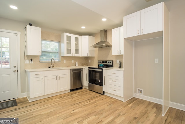 kitchen featuring light wood-type flooring, stainless steel appliances, sink, wall chimney range hood, and white cabinetry