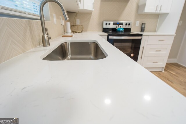 kitchen featuring white cabinetry, backsplash, stainless steel electric range oven, and sink