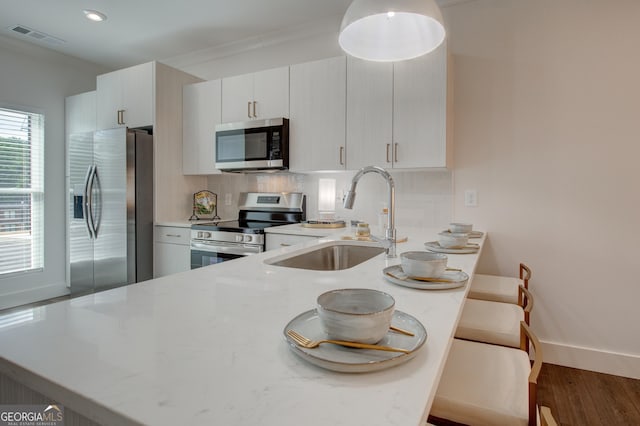 kitchen with kitchen peninsula, stainless steel appliances, decorative backsplash, white cabinetry, and sink