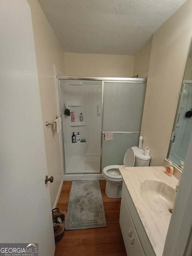 bathroom with vanity, a shower with door, hardwood / wood-style flooring, toilet, and a textured ceiling