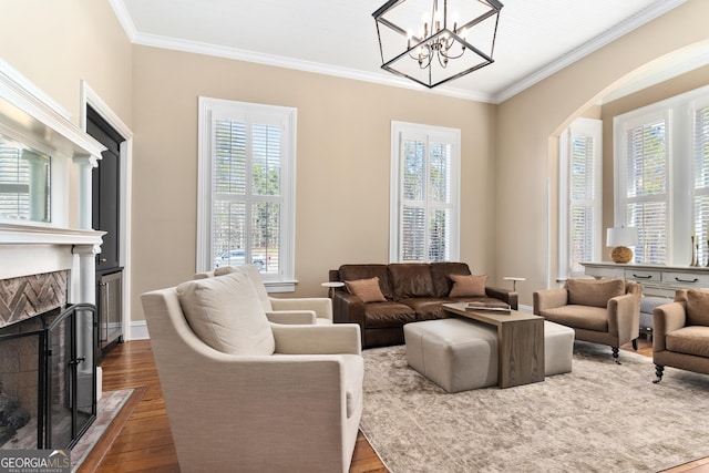 living room with wood-type flooring, ornamental molding, a tile fireplace, and a chandelier