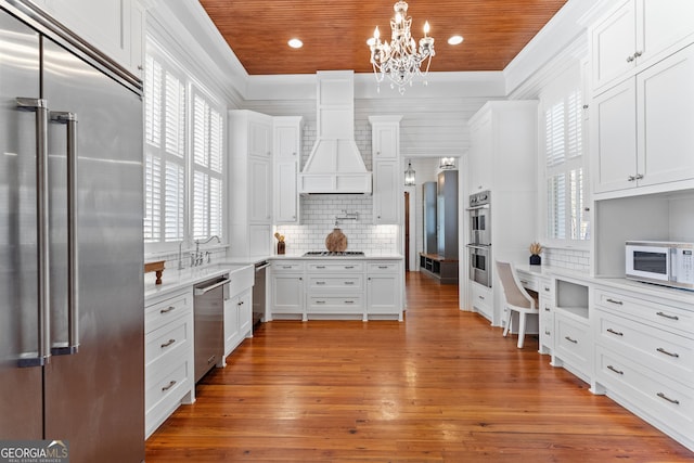 kitchen featuring pendant lighting, wooden ceiling, white cabinets, appliances with stainless steel finishes, and custom range hood