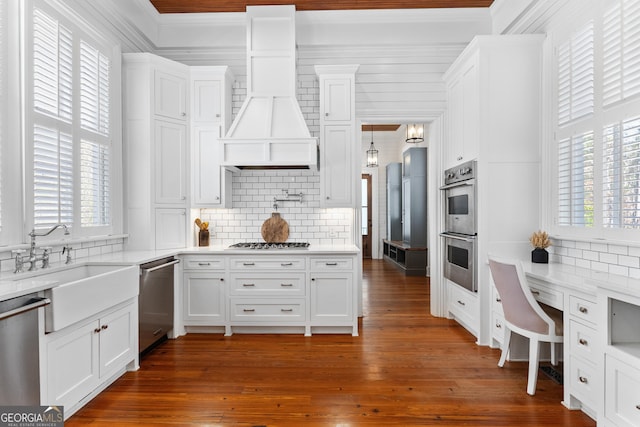 kitchen with custom exhaust hood, dark hardwood / wood-style floors, appliances with stainless steel finishes, tasteful backsplash, and white cabinetry