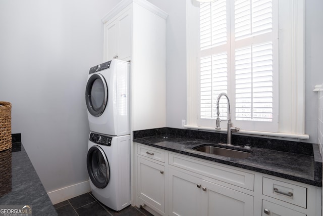 washroom featuring stacked washer / dryer, sink, cabinets, and dark tile patterned flooring