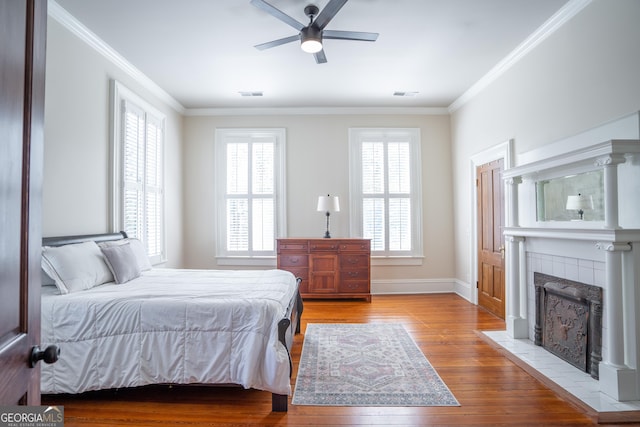 bedroom with light hardwood / wood-style floors, ceiling fan, ornamental molding, and a tiled fireplace