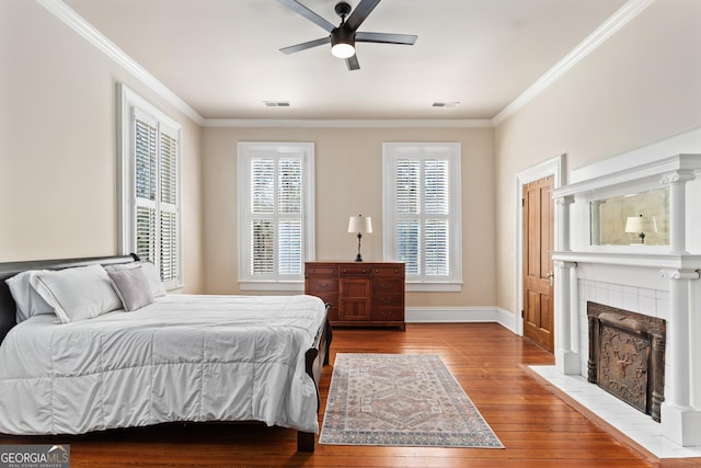 bedroom featuring a tile fireplace, ceiling fan, crown molding, and light hardwood / wood-style floors