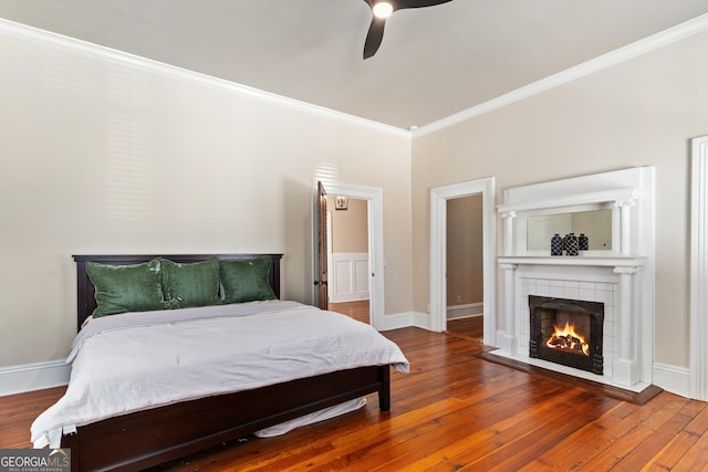 bedroom with a tile fireplace, hardwood / wood-style flooring, ceiling fan, and ornamental molding