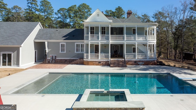 rear view of house with a patio area, a balcony, and a pool with hot tub