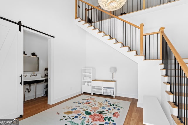 staircase with a barn door, a chandelier, wood-type flooring, and a high ceiling