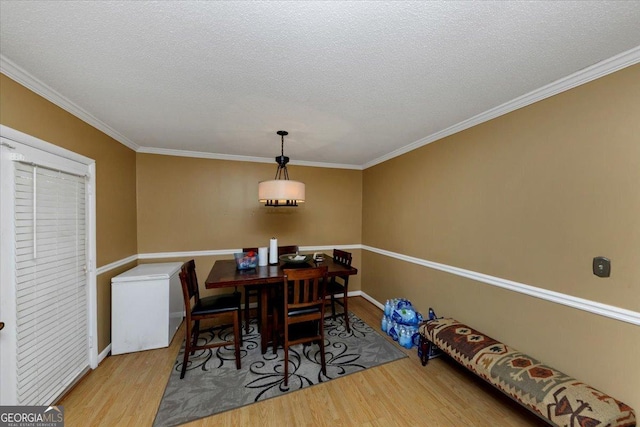 dining area with light hardwood / wood-style floors, ornamental molding, and a textured ceiling