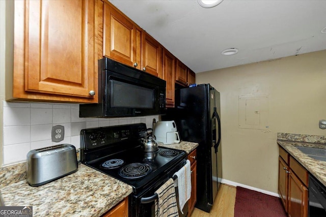 kitchen featuring decorative backsplash, light stone countertops, black appliances, and light hardwood / wood-style floors