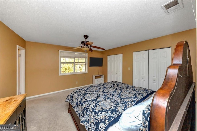 carpeted bedroom with two closets, ceiling fan, and a textured ceiling