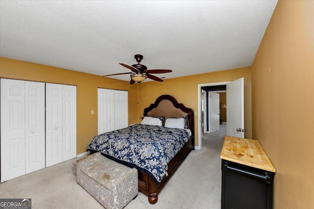 bedroom featuring two closets, ceiling fan, light carpet, and a textured ceiling