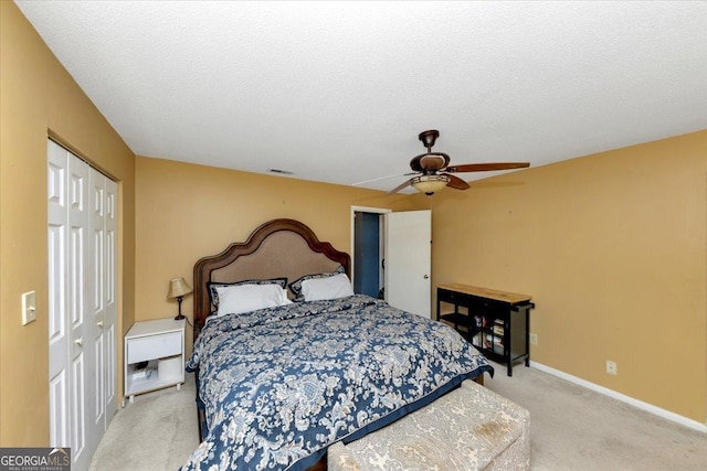 bedroom featuring ceiling fan, light colored carpet, a textured ceiling, and a closet