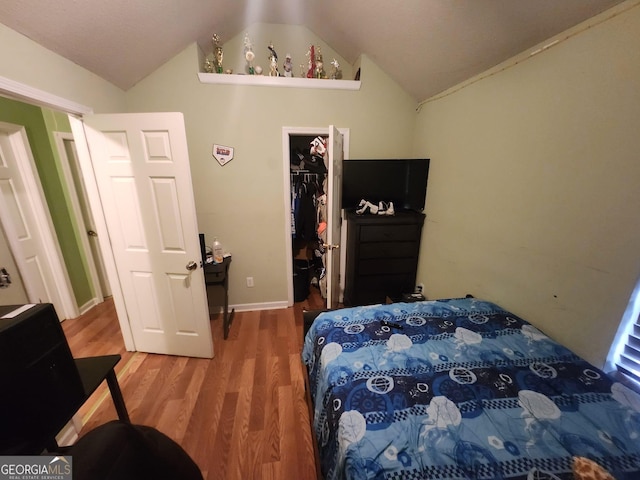 bedroom with a walk in closet, hardwood / wood-style flooring, vaulted ceiling, and a closet