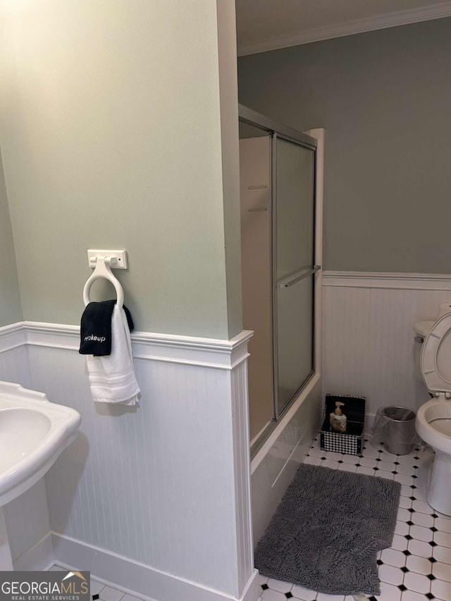 bathroom featuring tile patterned floors, toilet, shower / bath combination with glass door, and ornamental molding