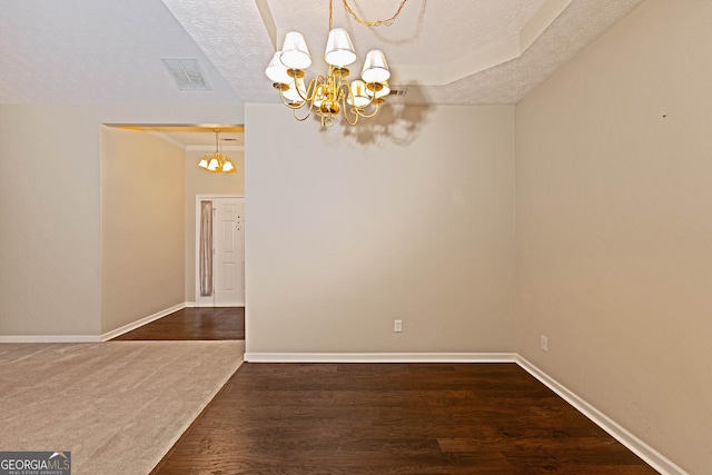 spare room with dark hardwood / wood-style floors, a textured ceiling, and an inviting chandelier