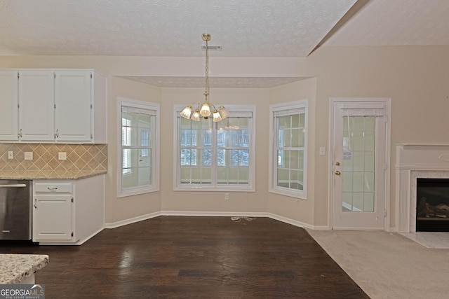 kitchen featuring tasteful backsplash, stainless steel dishwasher, pendant lighting, a fireplace, and white cabinets