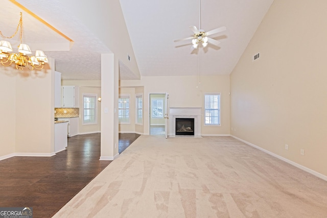 unfurnished living room featuring a fireplace, high vaulted ceiling, ceiling fan with notable chandelier, and hardwood / wood-style flooring