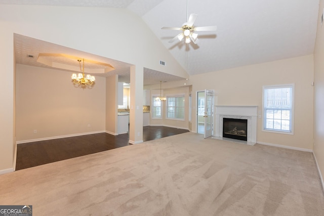 unfurnished living room with carpet flooring, ceiling fan with notable chandelier, vaulted ceiling, and a premium fireplace