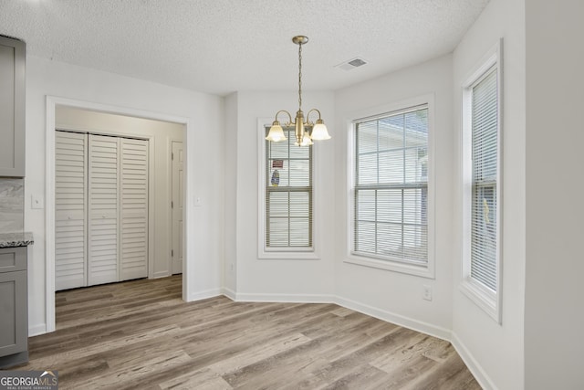 unfurnished dining area featuring light hardwood / wood-style floors, a textured ceiling, and a notable chandelier