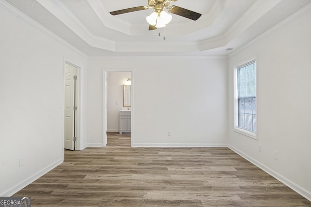 empty room featuring ceiling fan, wood-type flooring, a tray ceiling, and ornamental molding