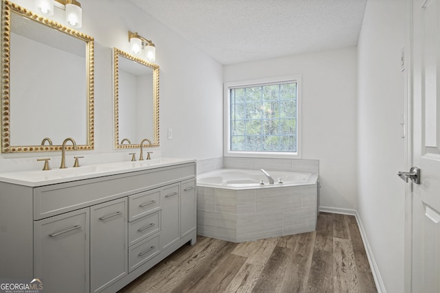 bathroom with a relaxing tiled tub, wood-type flooring, vanity, and a textured ceiling