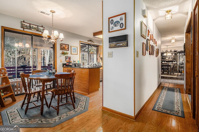 dining room featuring a textured ceiling, a notable chandelier, and light hardwood / wood-style flooring