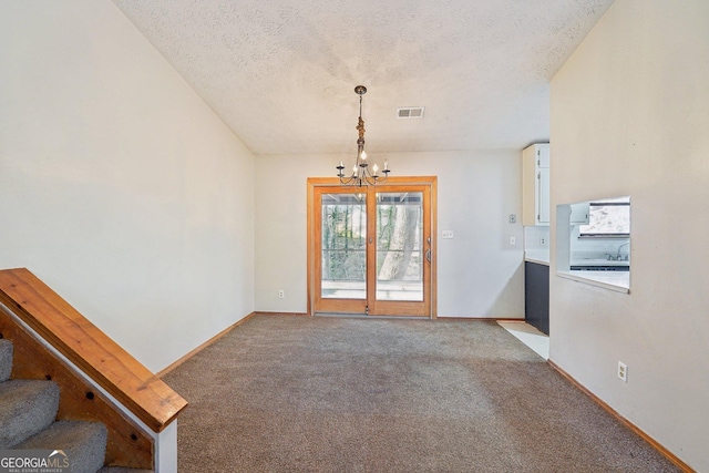 unfurnished room with a textured ceiling, carpet flooring, and a chandelier