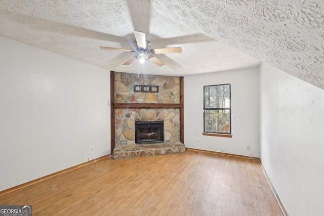 unfurnished living room with a textured ceiling, ceiling fan, hardwood / wood-style floors, and a stone fireplace