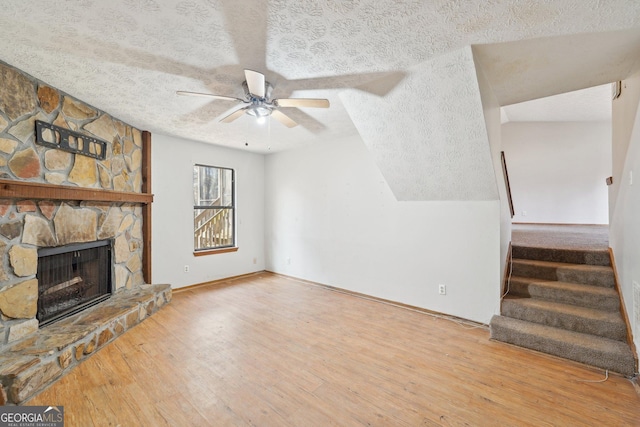 unfurnished living room featuring ceiling fan, light wood-type flooring, a stone fireplace, and a textured ceiling