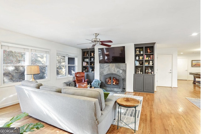 living room featuring built in features, light hardwood / wood-style flooring, and ceiling fan