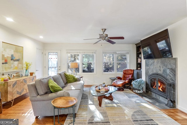 living room with ceiling fan, a premium fireplace, and light hardwood / wood-style flooring