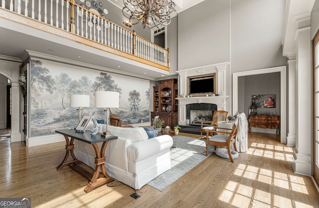 living room featuring an inviting chandelier, crown molding, hardwood / wood-style flooring, ornate columns, and a towering ceiling