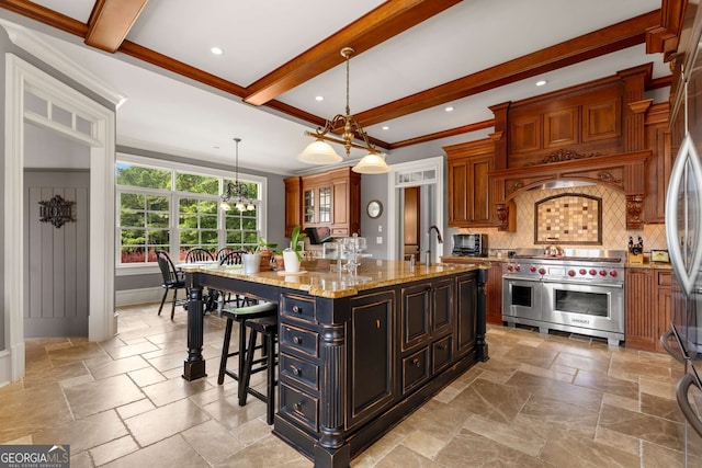 kitchen featuring light stone countertops, ornamental molding, a kitchen island with sink, double oven range, and hanging light fixtures