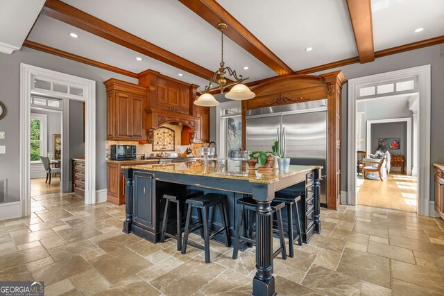 kitchen featuring light stone countertops, a breakfast bar, beam ceiling, a center island with sink, and hanging light fixtures