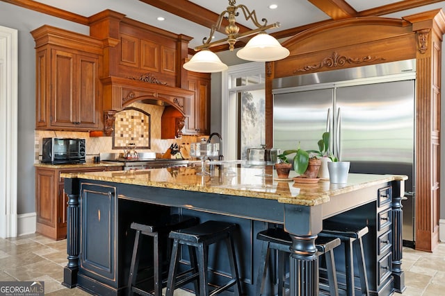 kitchen featuring stainless steel built in fridge, light stone counters, decorative light fixtures, a center island with sink, and range