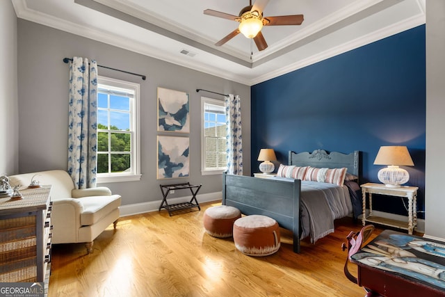 bedroom with a tray ceiling, ceiling fan, crown molding, and light hardwood / wood-style flooring