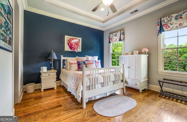 bedroom with ceiling fan, a raised ceiling, wood-type flooring, and crown molding