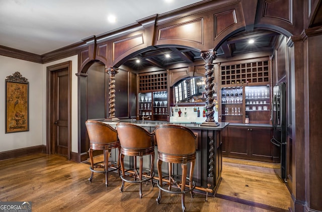 bar featuring hardwood / wood-style floors, decorative columns, black fridge, and crown molding