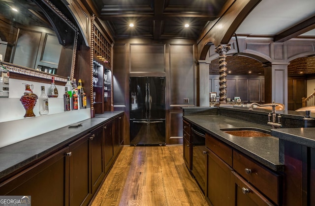 bar featuring coffered ceiling, black appliances, wooden walls, ornate columns, and beamed ceiling