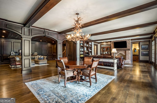 dining area with ornate columns, an inviting chandelier, dark hardwood / wood-style flooring, beamed ceiling, and a fireplace